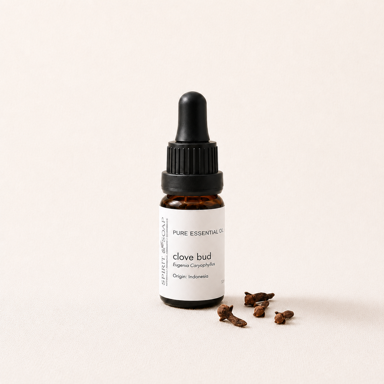 A small amber glass dropper bottle labeled 'PURE ESSENTIAL OILS clove bud' with a black dropper cap, photographed on a clean off-white background with a few loose cloves beside it.