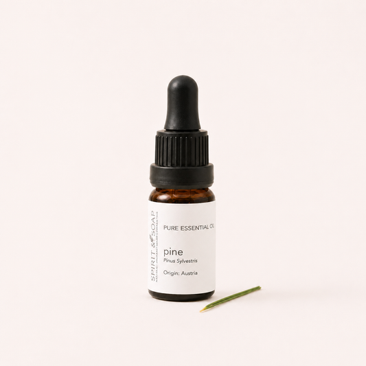A small amber glass dropper bottle labeled 'pine' essential oil by Spirit of Scalin, with a black dropper cap and a single pine needle placed in front, on a clean off-white background.